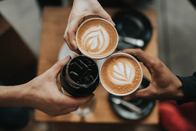Mehrere Hände halten Cappuccino-Tassen mit Latte Art
