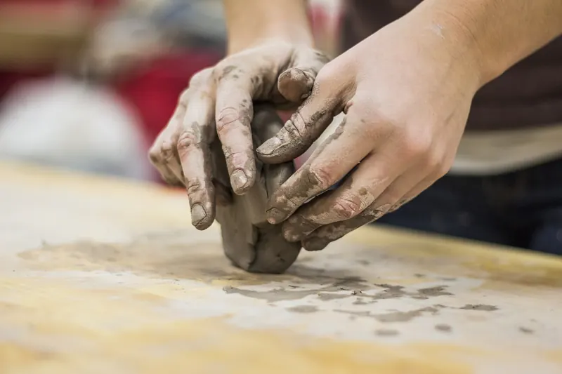 Hände formen einen Klumpen Ton auf einem Holztisch